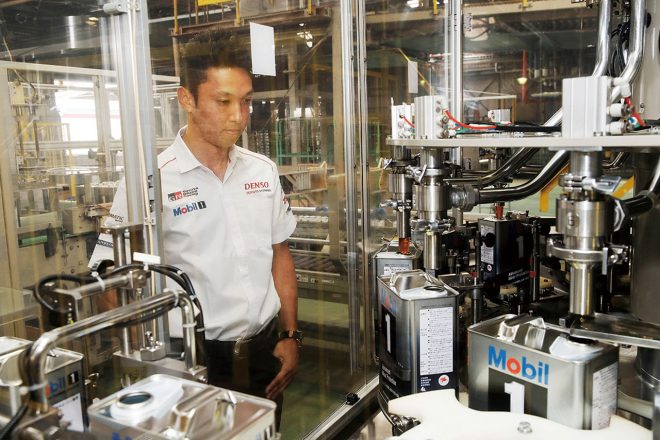 オイルが缶に充填されていくラインを見る一貴。「まったくこぼれない。よく出来ていますよね」。ここでは、4リッター缶の場合、1時間あたり2400缶（400ケース）を製造している。鶴見潤滑油工場全体では4ℓ缶換算で1年間に3000万台分のオイルを作っている。