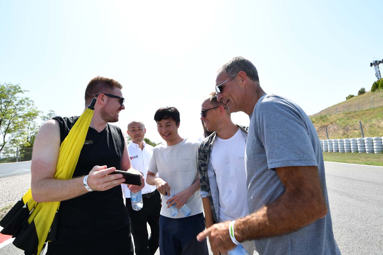 エンジニアのスマホを覗き込み笑顔を見せるハイクラス・レーシングのドライバーたち