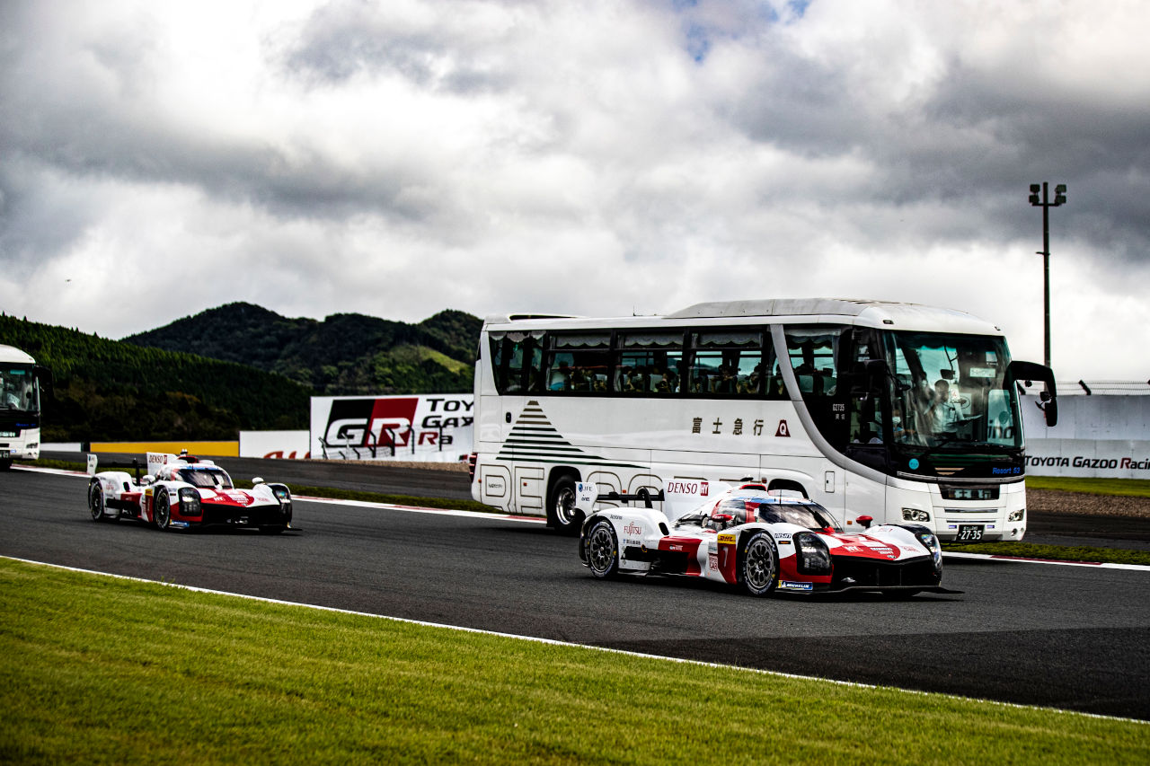 サーキットサファリで観光バスの脇を追い抜いていくトヨタGR010ハイブリッド　2022年WEC第5戦富士6時間